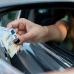 A-womans-hand-reaches-out-of-a-car-window-holding-two-drivers-licenses