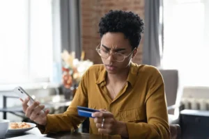 A-woman-with-a-concerned-look-on-her-face-holds-her-phone-in-one-hand-and-a-credit-card-in-the-other-after-being-scammed-through-a-cash-app-like-Zelle