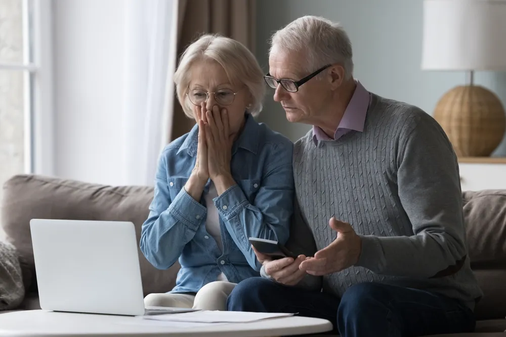 An_elderly_man_and_woman_look_shocked_at_their_computer_screen_possibly_because_they_are_victims_of_elder_fraud