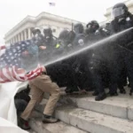 A_Clash_Between_Police_and_Rioters_on_Jan._6_with_Police_Officers_Spraying_a_Man_Approaching_Them_Carrying_an_American_Flag_The_Daily_Muck