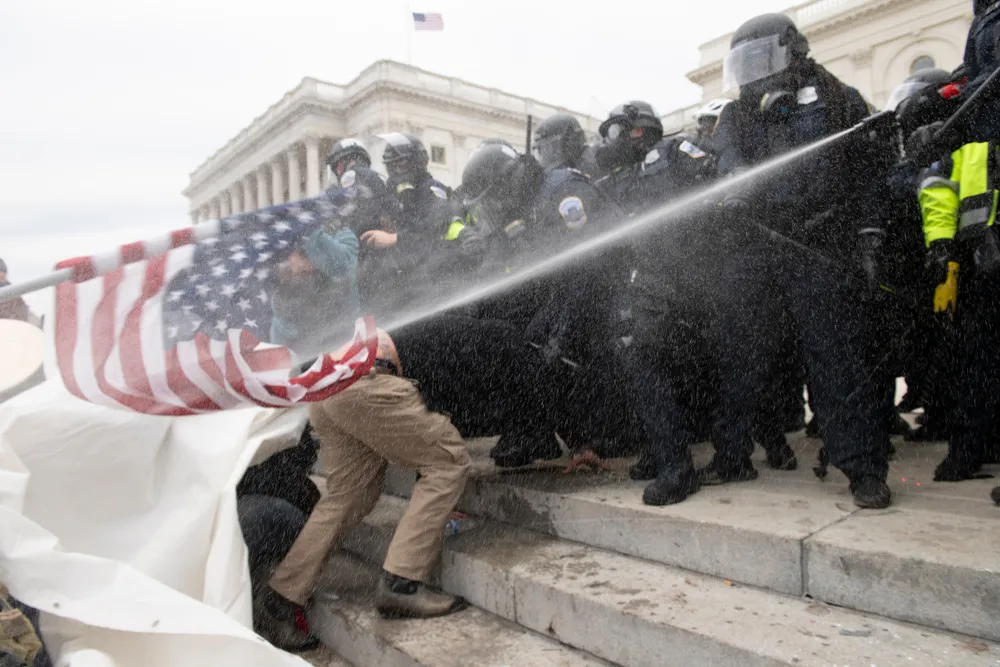 A_Clash_Between_Police_and_Rioters_on_Jan._6_with_Police_Officers_Spraying_a_Man_Approaching_Them_Carrying_an_American_Flag_The_Daily_Muck