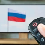 A_Person_Holds_a_Remote_Control_in_Front_of_a_Television_with_The_Russian_Flag_The_Daily_Muck