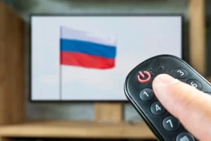 A_Person_Holds_a_Remote_Control_in_Front_of_a_Television_with_The_Russian_Flag_The_Daily_Muck