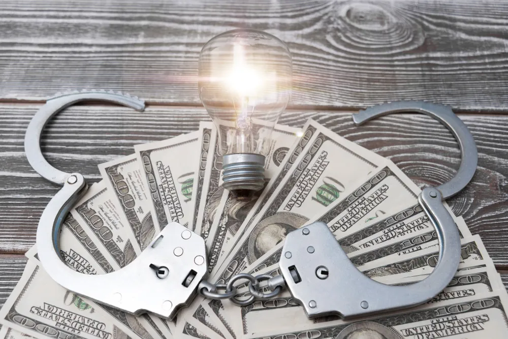 A_Lightbulb_and_a_Pair_of_Handcuffs_on_a_Pile_of_Money_Represents_Jonathan_Freezes_Guilty_Plea_for_Defrauding_Green_Energy_Investors