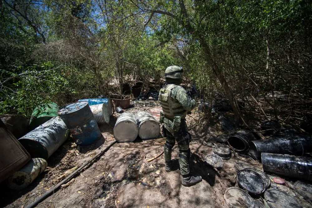 A Man in Military Dress Holds a Rifle Near Empty Barrels Where Drugs Were Stored in Sinaloa - The Daily Muck