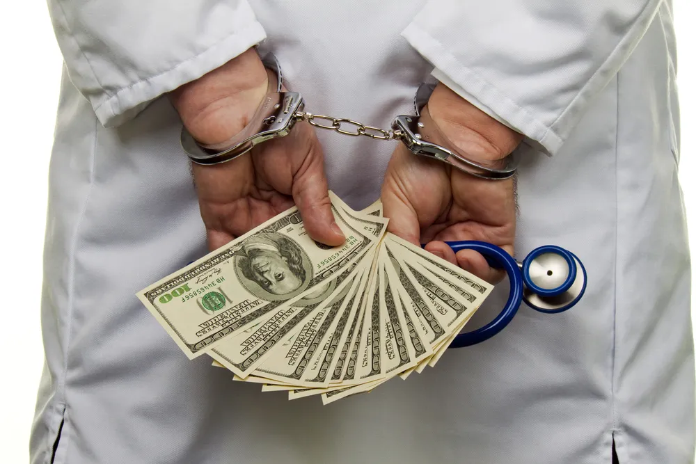 A Man In a Lab Coat With His Hands Behind His Back and Holding 1000 in 100 Bills.