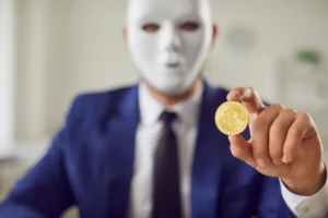 A_Man_With_A_Blurred_Masked_Face_Holds_Up_a_Gold_Coin_Representing_a_Bitcoin_Which_Richard_Appelbaum_Used_to_Launder_Stolen_Money