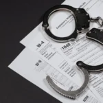 A_Pair_of_Handcuffs_on_Top_of_U.S._Tax_Forms_Represent_Shandel_Arkadie_Who_This_Week_Admitted_to_Failing_to_Pay_1.5_Million_in_Employment_Taxes