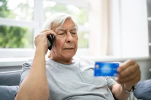 An_Elderly_Man_Looks_at_His_Credit_Card_While_Talking_on_the_Phone_Representing_Tech_Fraud_Scams_AllegeDly_Commited_by_Sun_Tong_Lin_and_Xueliang_Chen_Both_From_Staten_Island