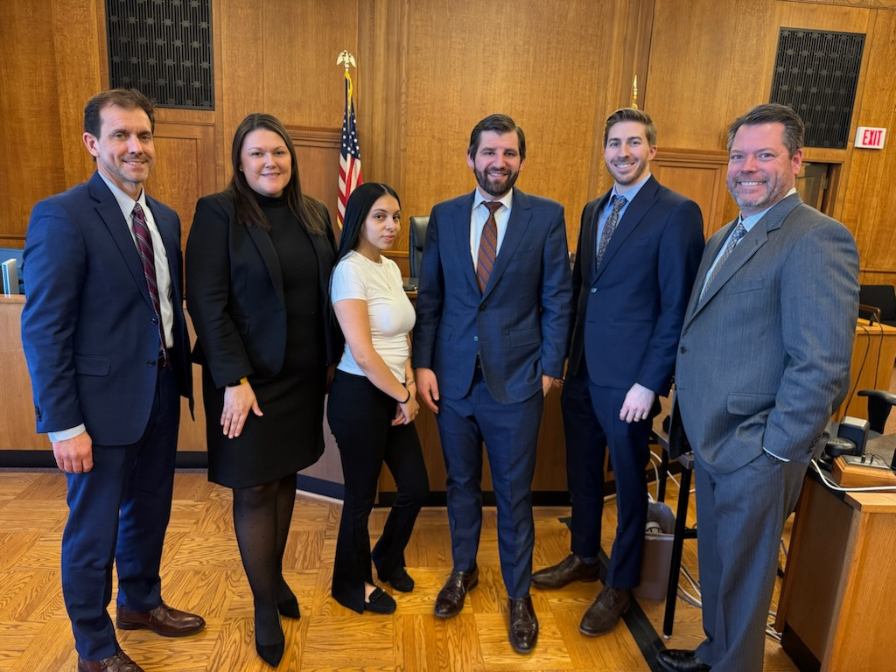 Monica Cerna standing with attorneys Gino Alia, Matthew Patterson, Ryan Timoney, Kevin Martin, and paralegal Allison Rogers in a courtroom after the trial.